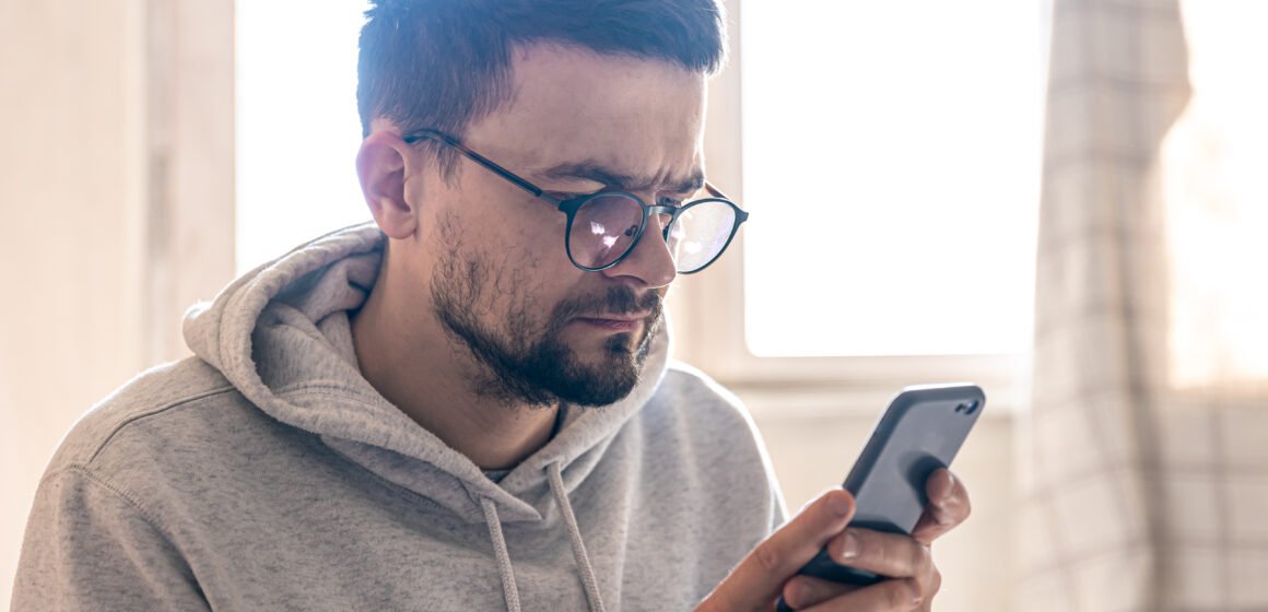 A man with glasses uses a smartphone, copy space. Com o fim das bets, especialista explica como reorganizar as finanças